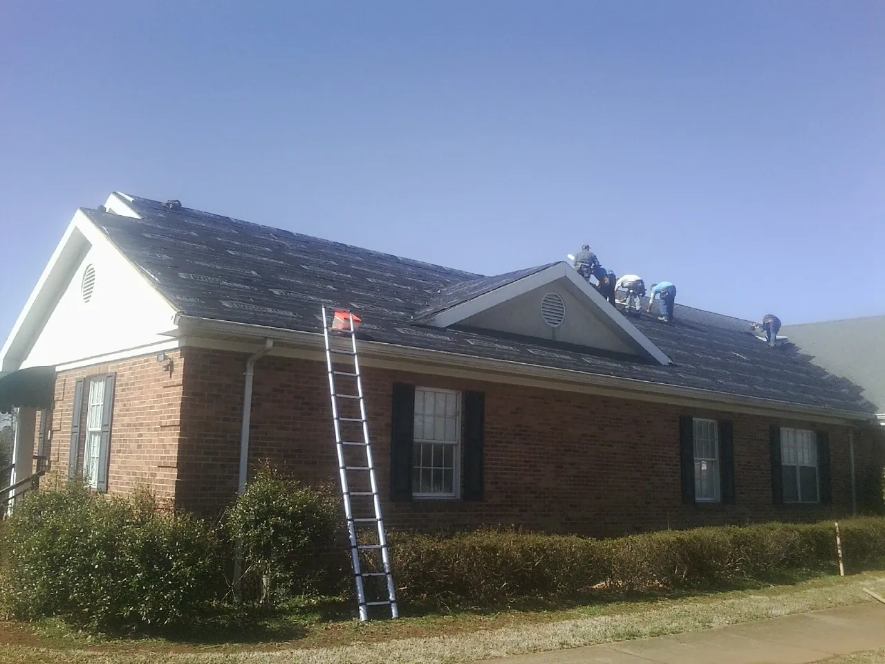 Crew tearing shingles off a brick ranch roof with a ladder set — Emergency Roof Repair work by our crew in Bolton
