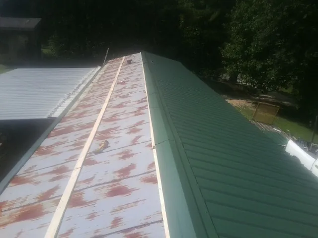 Old rusted panels beside newly installed green metal roofing — Wind Damage Roof Repair by Roofing Brothers in Bolton